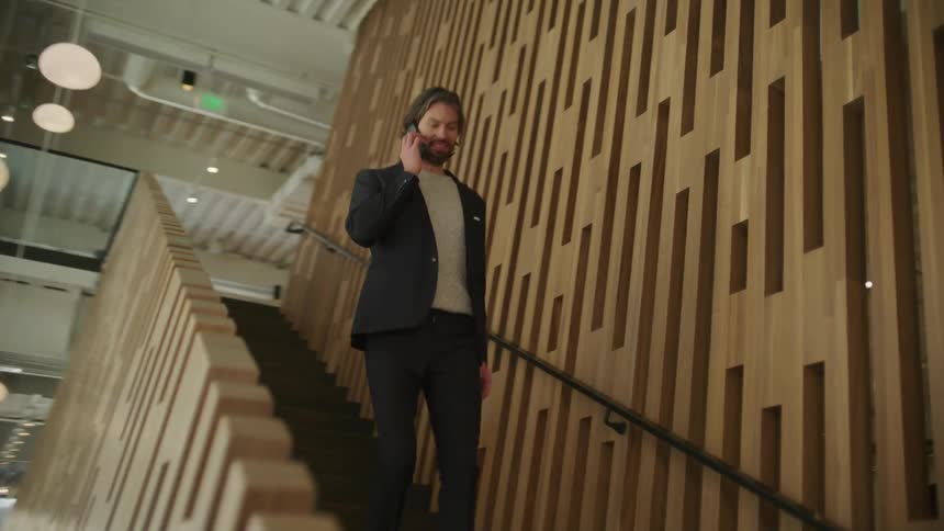A man talks on the phone while jogging down the steps in an office