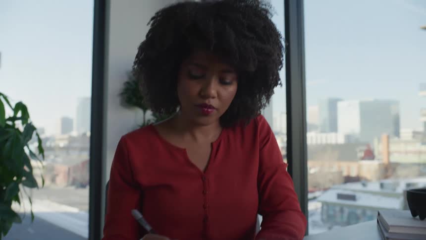 A woman typing on a laptop and taking notes while working in an office