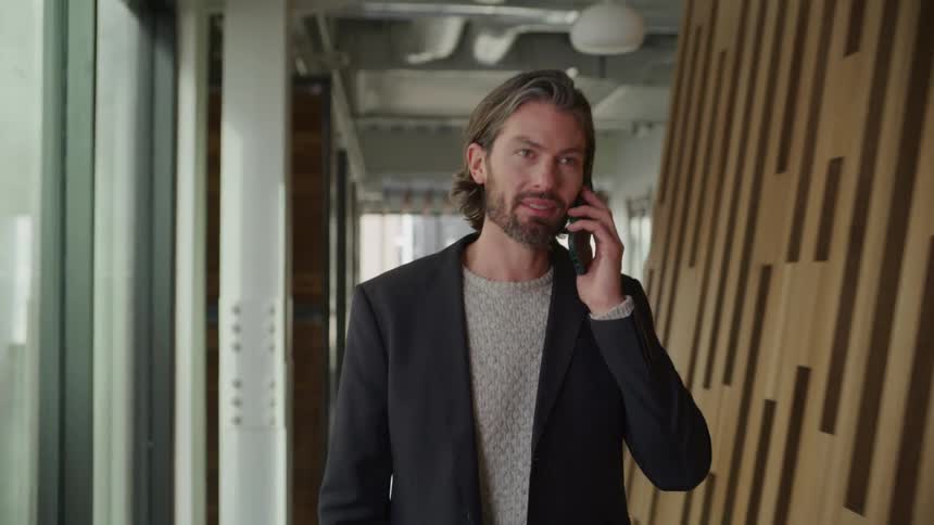 A man texting and then talking on the phone while walking through a corridor