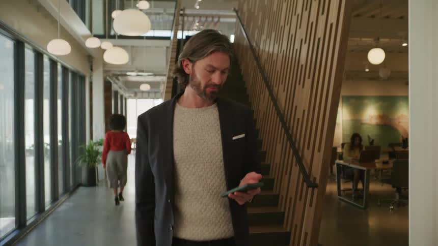 A man walking down the stairs while looking at his phone and walking forward