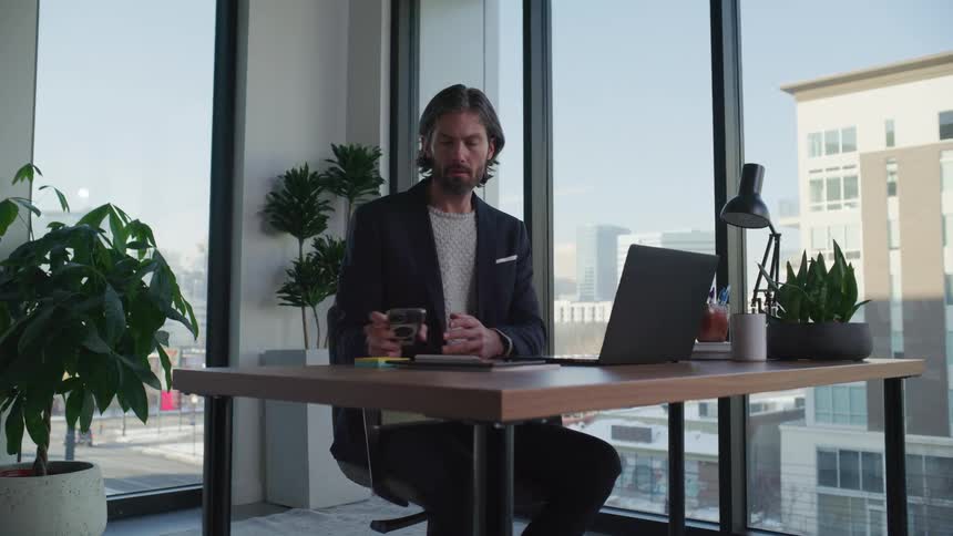Man working in office checks phone then glances out window