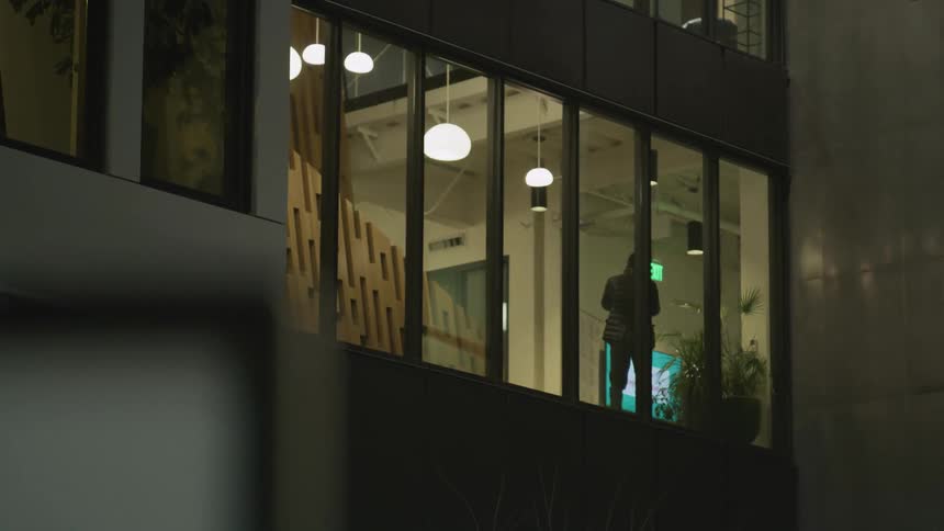 An outside of a building looking in at a man walking by windows on his phone