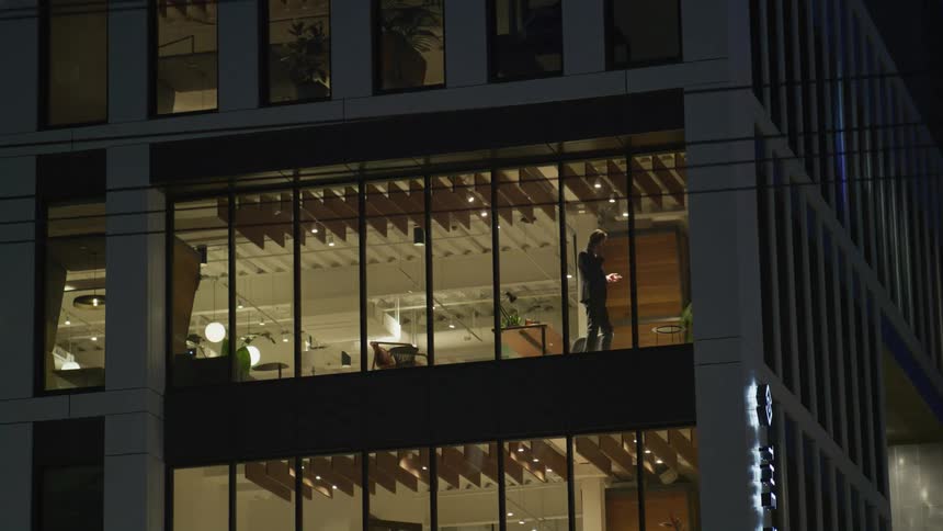 A man talking on his phone pacing back and forth in front of a window