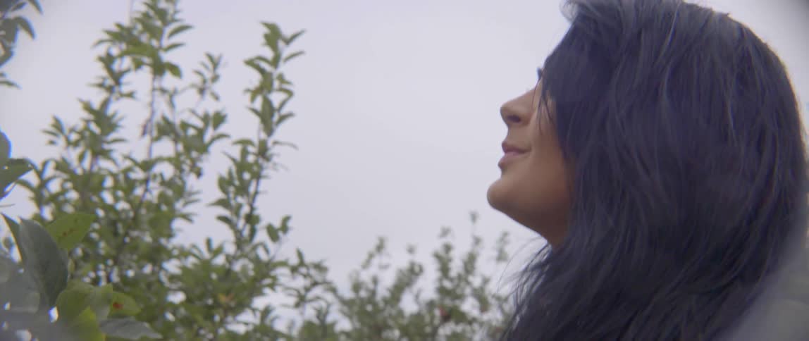 A happy woman smiles while surveying rows of productive apple trees in an orchard.