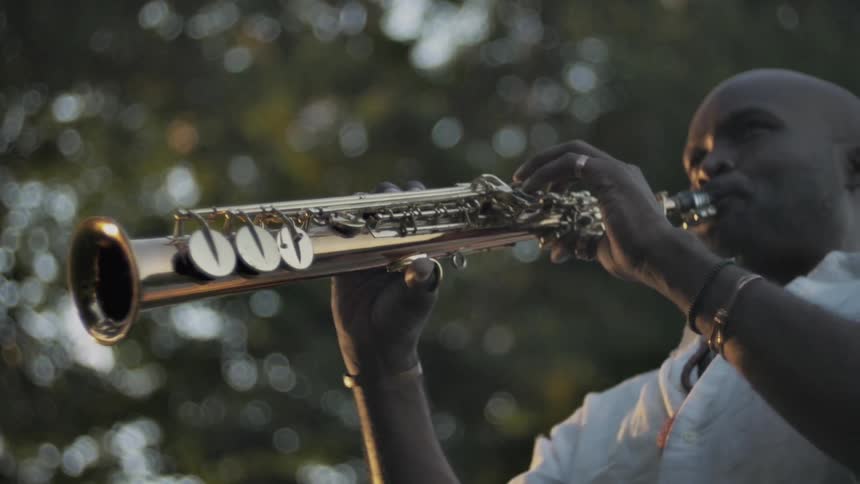 A trumpet player plays his instrument under trees