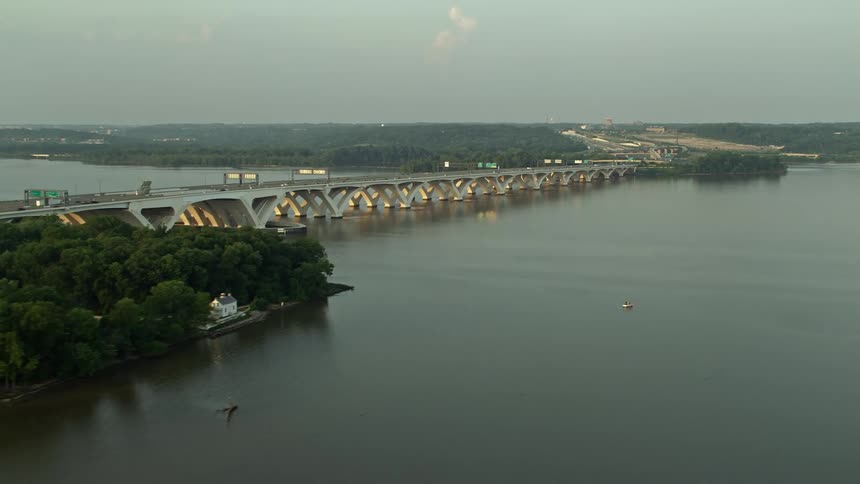 An aerial view of the Woodrow Wilson Bridge over the Potomac River at sunset showing traffic moving across it in and out of downtown