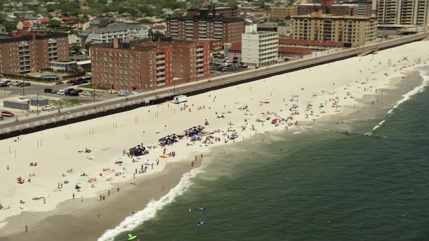 Aerial footage tilting down to a crowded beach of sunbathers enjoying the sunshine and coastline in Long Beach New York