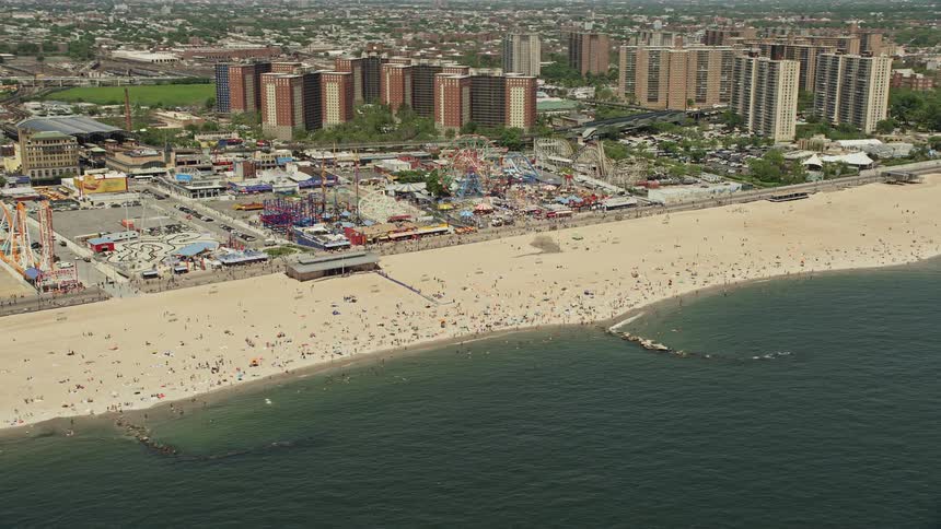 Aerial footage of a bustling Coney Island Beach with sunbathers and Luna Park in the background