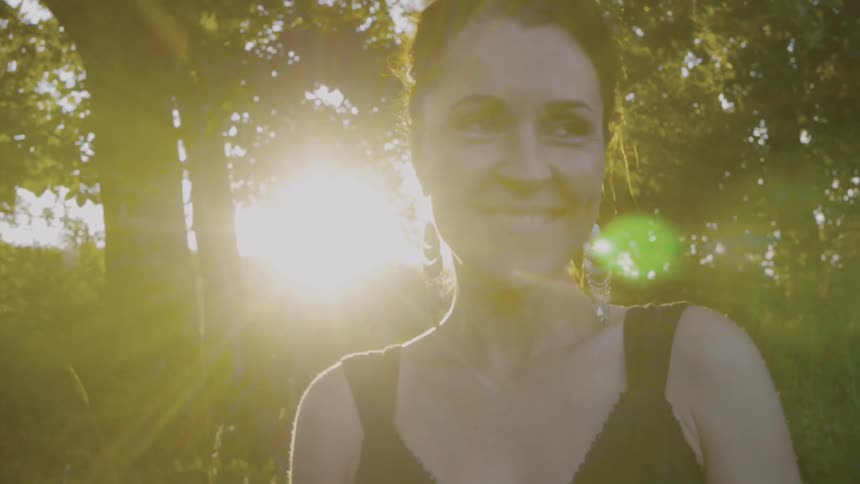 A woman stands near trees on a sunny day