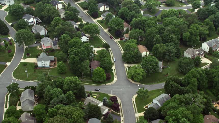 Aerial view of a suburban neighborhood in Burke Virginia tilting down from the clouds showcasing lush tree-lined streets and single-family homes