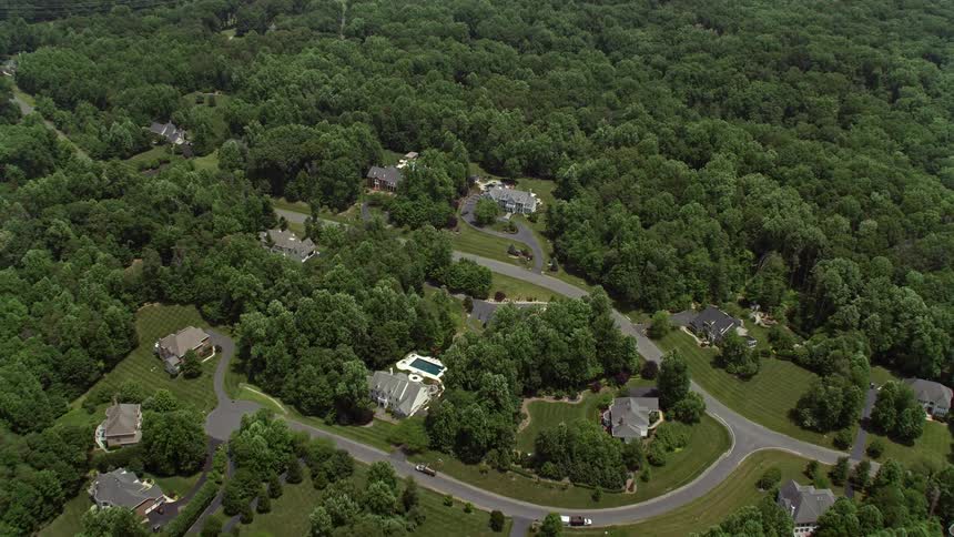 Aerial footage of luxurious homes in Clifton Virginia with a tilt down to showcase one of the estates surrounded by trees and a swimming pool on a sunny day in the summer