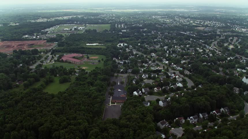 Flying over rural homes and farmland in Manassas Virginia this aerial footage captures the countryside approach towards Prince William Parkway on a hazy day during spring or summer