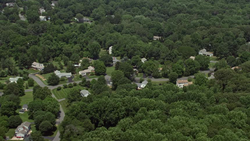 Flying over suburban homes and green trees in Clifton Virginia during sunny daytime in the summer