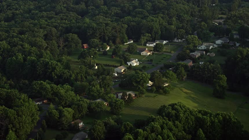 Flying over rustic homes nestled in rural neighborhoods surrounded by a forest canopy at sunset in Manassas Virginia