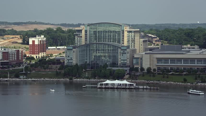 Approaching the Gaylord National Resort & Convention Center in National Harbor Maryland via aerial footage on a hazy summer day with boats traveling in the harbor