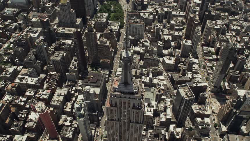 An aerial view of the Empire State Building and towering skyscrapers in Midtown Manhattan New York City shot from a birds eye perspective tilting down towards the city