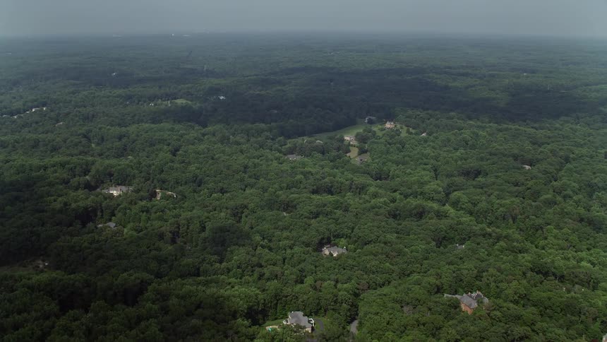 Approaching upscale homes surrounded by deciduous trees in Clifton Virginia during daytime aerial footage