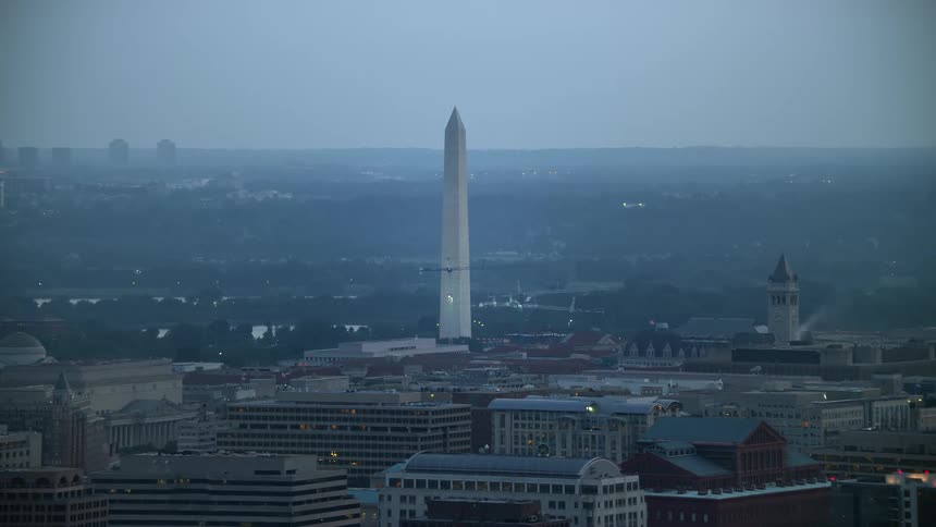 Aerial footage of Washington Monument during twilight set against the hazy backdrop of Washington DCs city buildings