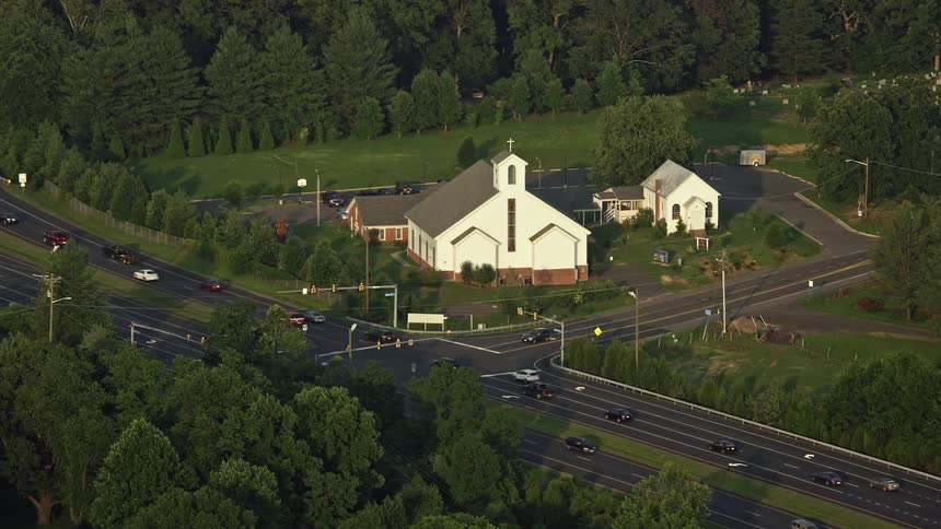 An aerial view of cars driving past Buckhall United Methodist Church at sunset in a rural area