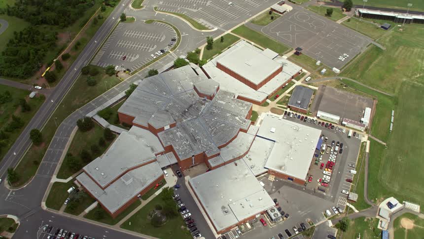 An aerial view tilts down to a birds-eye view of a large high school in Manassas Virginia during the daytime with partly cloudy skies