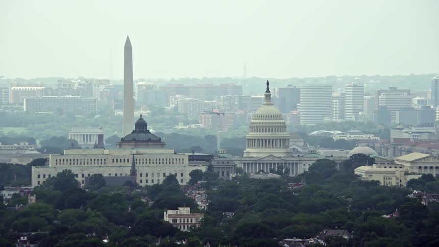 Aerial footage of Washington DCs landmarks including the Washington Monument Library of Congress buildings and United States Capitol Dome shot during a hazy summer day