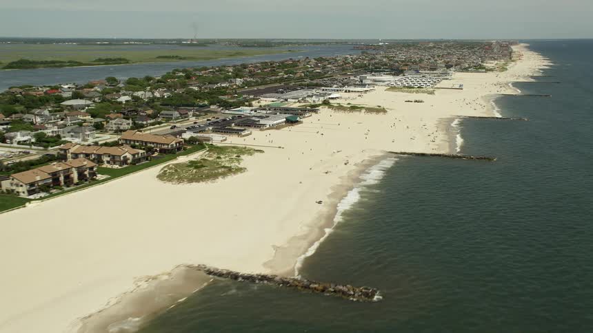 Aerial footage passing by Atlantic Beach apartment complex and crowded beachgoers enjoying the sunshine over the picturesque coastline of Long Island New York