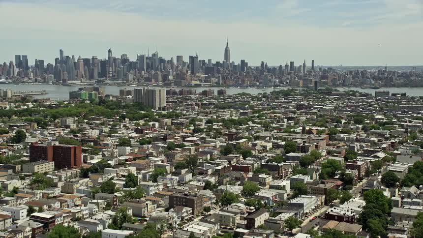 A stunning aerial view of Midtown Manhattan skyline seen from Jersey City urban neighborhoods with the Hudson River and New York City in the backdrop during a sunny day
