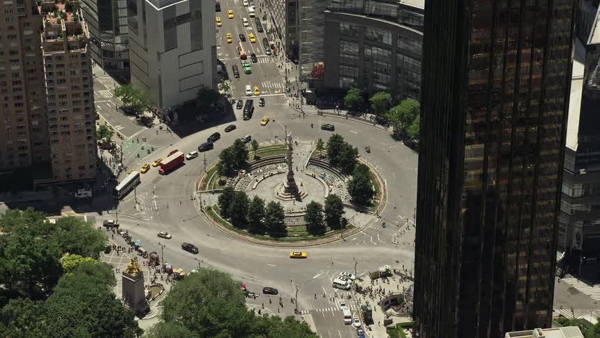 Approaching and tilting down to Columbus Circle a famous intersection in Midtown Manhattan with skyscrapers and cars travelling around in a sunny daytime aerial view during summer