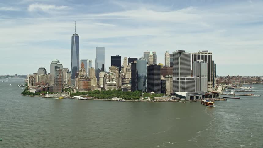 Aerial footage of Lower Manhattan skyline and Battery Park on a sunny day in New York City with views of skyscrapers city parks and the Staten Island Ferry Terminal