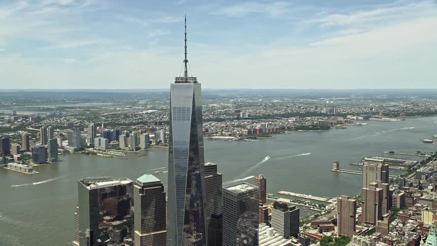 Tilting down aerial footage of One World Trade Center revealing World Trade Center Memorial and Lower Manhattan on a partly cloudy day