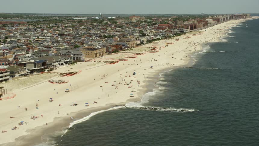 Aerial footage captures the beautiful Long Beach coastline and beachfront neighborhoods on a sunny day in New York bustling with beachgoers enjoying various recreational activities