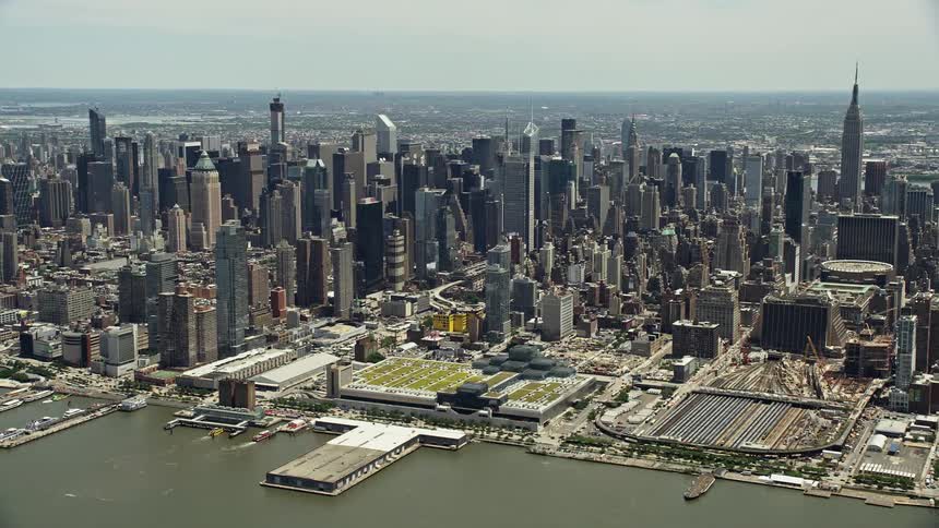 A stunning aerial footage of the Hudson Yards and Hells Kitchen in Midtown Manhattan showcasing the towering high rises and bustling transit systems during daytime