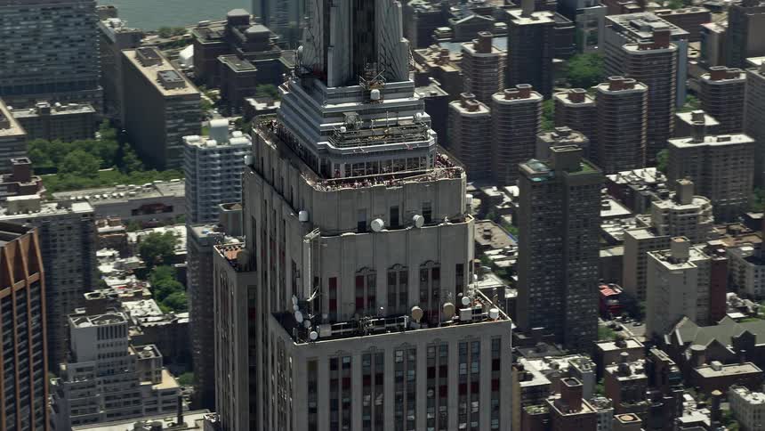 Aerial footage of the upper levels of the iconic Empire State Building and surrounding skyscrapers in Midtown Manhattan New York City captured during a sunny summer day
