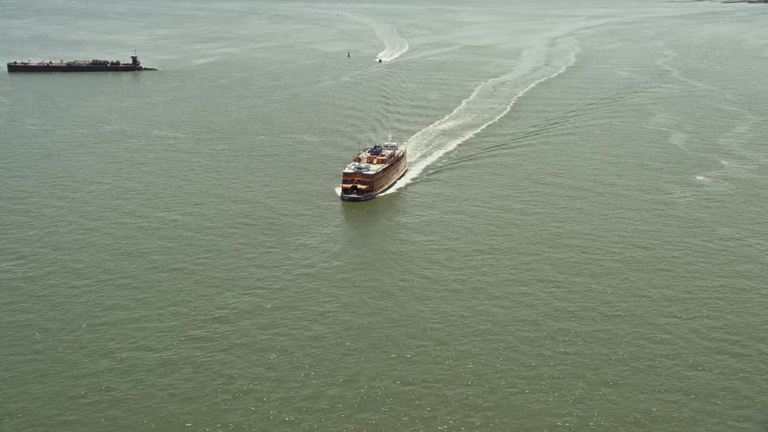 Aerial footage of Staten Island Ferry sailing through New York Harbor with city bridge in the background
