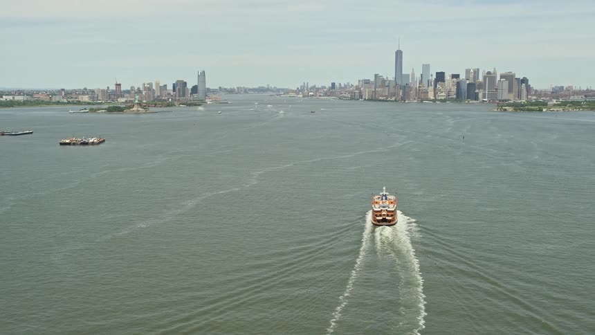 Aerial footage of the Staten Island Ferry on New York Harbor tilting up to reveal the skylines of Jersey City and Lower Manhattan on a sunny day showcasing the bustling transportation and shipping industry of the metropolitan areas