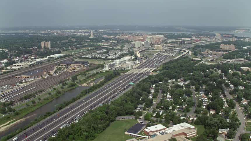 Aerial footage of traffic moving on Interstate 95 between train yard and suburban homes in Alexandria Virginia on a hazy day surrounded by residential areas and office buildings