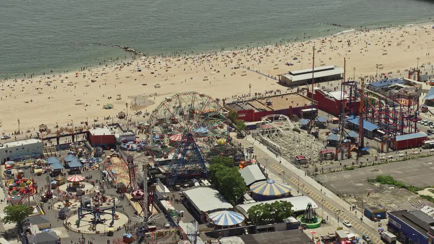 An aerial view of Luna Parks Ferris wheel and a crowded Coney Island Beach on a sunny day in New York City during summer