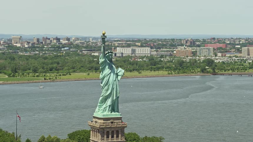 Aerial footage of the Statue of Liberty overlooking New York Harbor with the cityscape in the background shot during summer