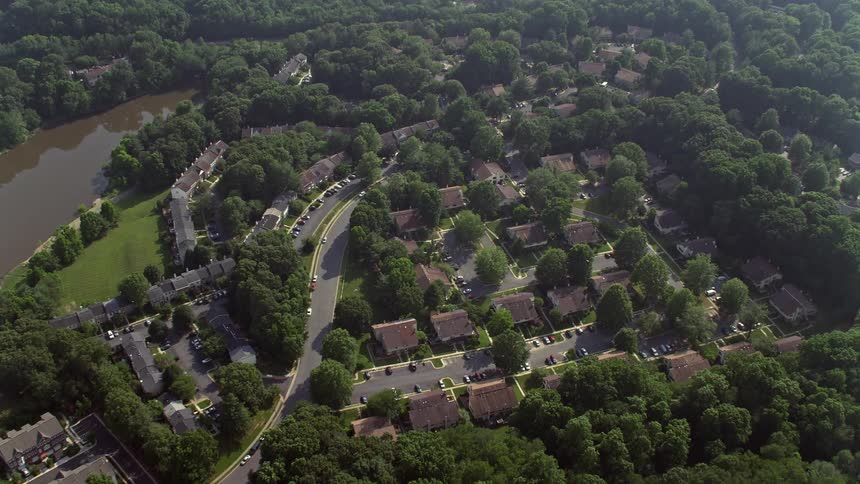An overhead daylight aerial shot tilts down to show a birds eye view of suburban tract and row houses beside Lake Barton in Burke Virginia during summer
