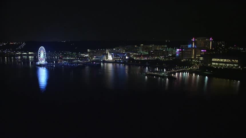 A stunning aerial view of the National Harbor Maryland skyline at night showcasing the Capitol Wheel apartment buildings and Gaylord National Resort and Convention Center amidst clear skies and waterways