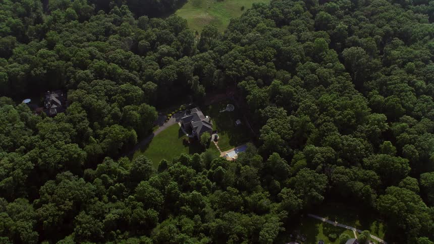 An upscale Virginia mansion with a stunning pool is shown from a birds eye view during a hazy daytime