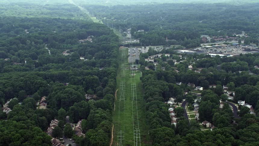 Aerial footage of power lines running through trees and suburban areas in Burke Virginia during the summer