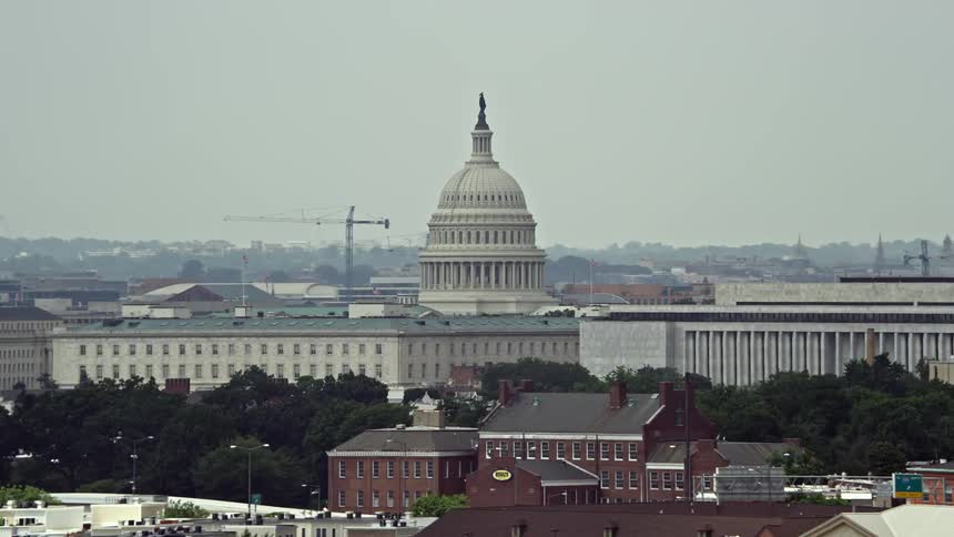 An iconic aerial view of the United States Capitol on Capitol Hill passing smoke stacks in Washington DC during daytime
