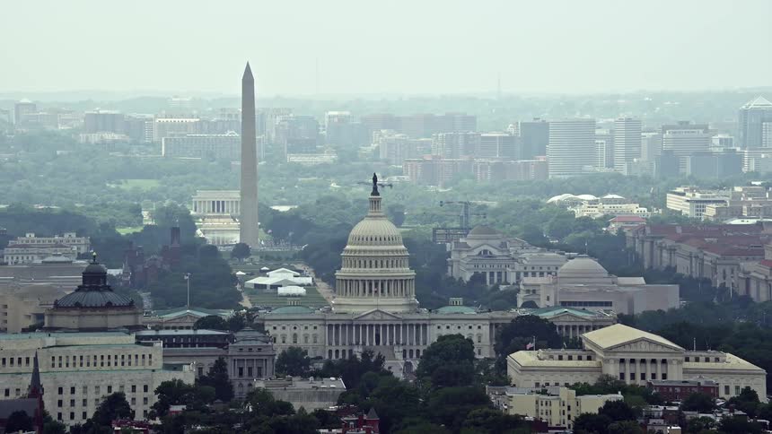 Aerial footage of the United States Capitol and National Mall in Washington DC including the Washington Monument and Lincoln Memorial captured on a hazy day during the summer months