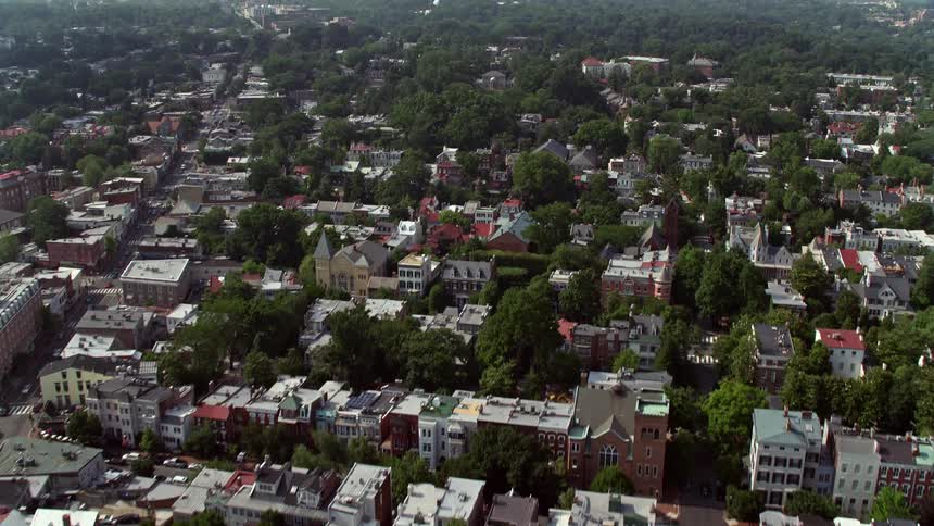 A stunning aerial footage flying over Georgetown Washington DC reveals the beautiful suburbs residential areas city buildings shops and the magnificent Washington National Cathedral on a sunny day