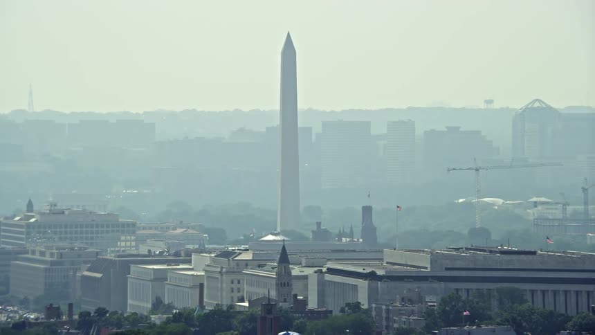 Aerial footage of the Washington Monument taken on a hazy day over rooftops in Washington DC