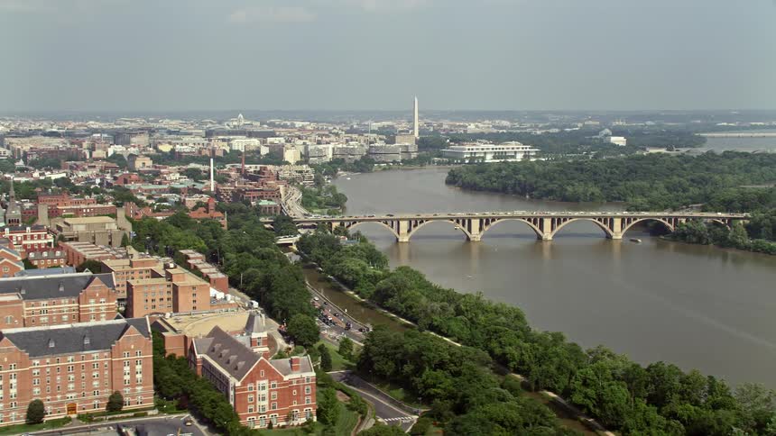 An aerial view of Washington DC during the summer showcasing the bridge over the Potomac River Georgetown University and the iconic Washington Monument towering in the distance