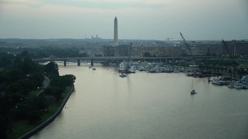 Approaching aerial footage of the Francis Case Memorial Bridge Washington Monument and marina near office buildings during twilight in Washington DC