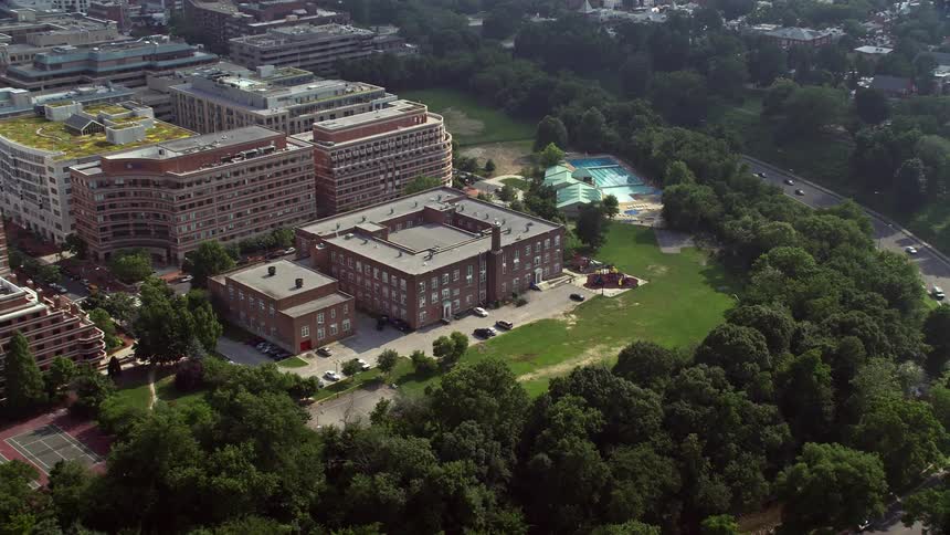 Aerial footage of Francis-Stevens Education Campus in Washington DC during a sunny daytime with trees and green grass around the building