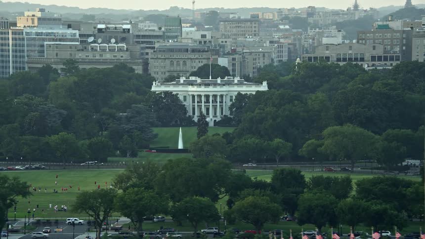 An aerial view at sunset of the iconic structures of the White House and Washington Monument in Washington DC with a hazy recreation atmosphere in the background